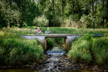 Twee rouwen fietsen over een brugje over de Demer